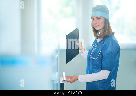Jeune femme médecin réfléchie dans un uniforme bleu debout à l'intérieur dans un dossier clinique, la mise en classeur Banque D'Images