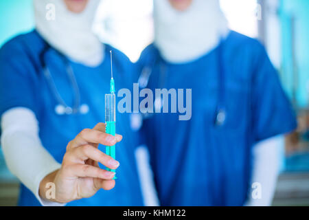 Deux jeunes femmes l'arabe les médecins en uniforme bleu et blanc et d'un hijab blanc, l'un d'entre eux détenant une injection, focus on hand Banque D'Images