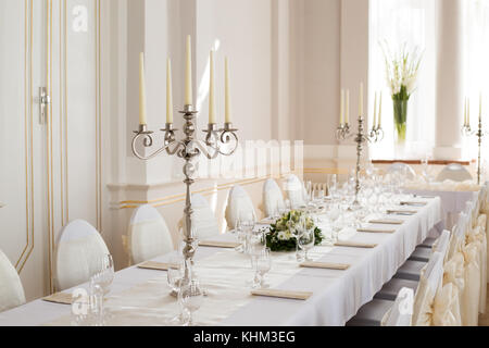 Photo en gros plan de chrome avec chandelier éteint cinq bougies en cire blanche placée sur la table préparée pour votre réception de mariage Banque D'Images