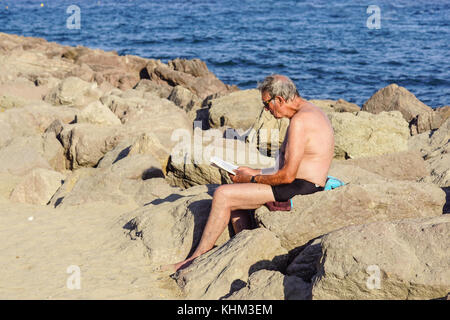 Nice , France - 5 août 2017 : vue de l'homme assis sur les rochers à se détendre et lire un livre sur la plage Banque D'Images