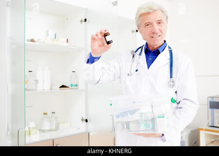 Homme mature en uniforme montrant une petite bouteille de pilules dans les cliniques Banque D'Images