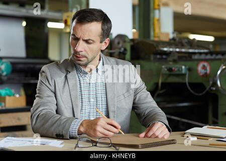 Se concentrant sur l'ingénieur faire des croquis dans le bloc-notes pendant la recherche de document Banque D'Images