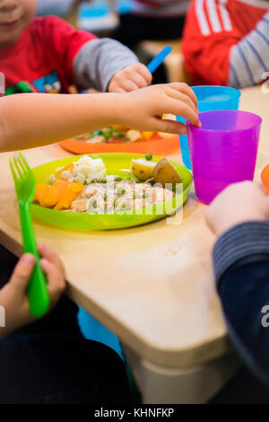 L'école d'avant garde pour les jeunes enfants : les jeunes enfants de manger leur repas à l'heure du dîner dans une crèche maternelle dans le pays de Galles UK Banque D'Images