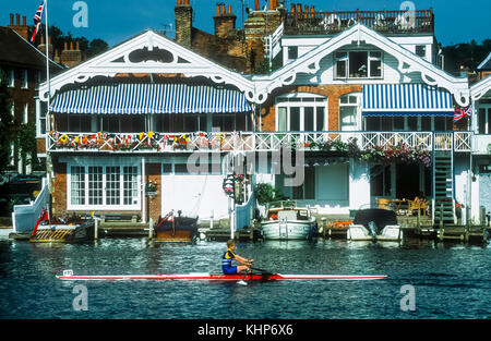 La rameuse navigue passé maisons sur thh waterfront au Henley on Thames. Banque D'Images