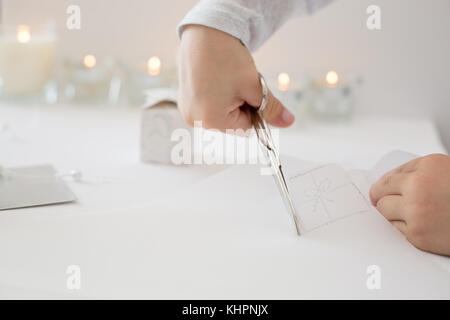 La photo en gros plan de l'enfant tenue de coupe ciseaux, papier blanc, la création d'origami papier de noel Banque D'Images