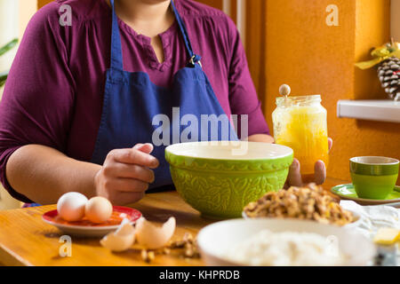 La photo en gros de jeunes femmes assis dans la cuisine, derrière une table de cuisine en bois, tenant un pot de miel à la main. En face d'elle, sur Banque D'Images