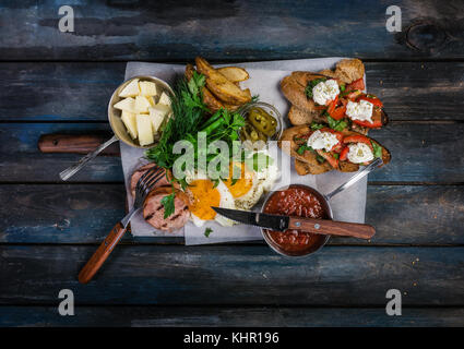 Grand petit-déjeuner. saucisses, brusquets, œufs frits, fromage de pommes de terre et les verts de sauce. Vue de dessus en bois de couleur arrière-plan. Banque D'Images