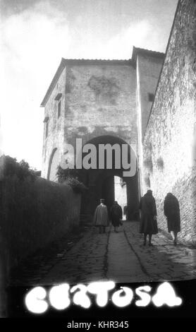 Années 1920, historique, des gens, y compris un homme avec une cape et un chapeau, sur une passerelle pavée extérieure à Certosa di Pavia, un complexe monastère à Certosa, Lombardie, Italie. Photographie prise lors d'un « Grand Tour », de vastes voyages touristiques européens effectués par les riches et leur entourage à cette époque. Banque D'Images