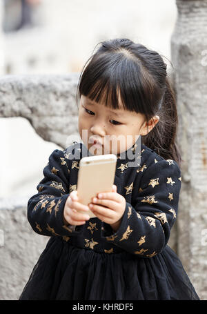 Xian, Chine - octobre 22,2017 : petite fille joue avec l'iphone dans la rue le 22 octobre, la Chine. Banque D'Images