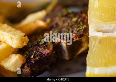 Délicieuse portion de succulentes grillades de grand T-bone steak assaisonné d'herbes méditerranéennes à côté de frites et de tranche de citron Banque D'Images