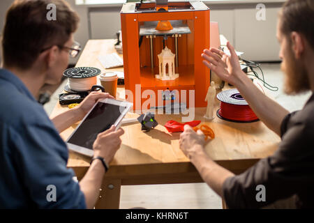 Vue arrière de jeunes ingénieurs talentueux assis à un bureau et l'exécution de l'inspection de la qualité du prototype mis avec l'aide de l'imprimante 3D, intérieur de moder Banque D'Images