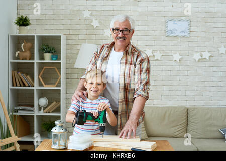 Portrait d'heureux grand-père posant avec petit-fils à la caméra et au sourire alors que le travail du bois à la maison Banque D'Images