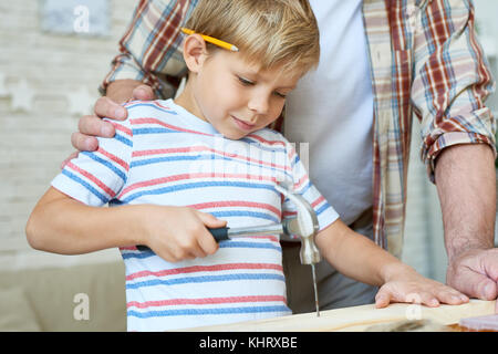 Closeup portrait of senior man helping little boy marteler les ongles tout en maquette en bois ensemble à la maison Banque D'Images