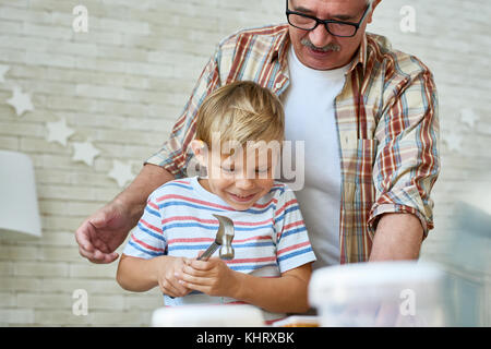 Portrait of smiling senior man helping little boy marteler les ongles tout en maquette en bois ensemble à la maison Banque D'Images