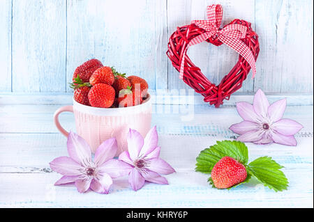 Deux coeurs de tissu avec une fraise mûre dans une tasse en céramique rose cadeau pour la Saint-Valentin sur un fond en bois bleu avec des fleurs délicates clemati Banque D'Images