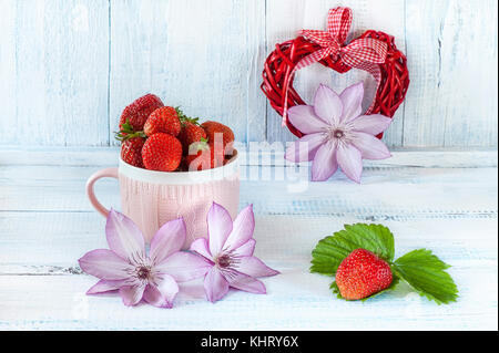 Deux coeurs de tissu avec une fraise mûre dans une tasse en céramique rose cadeau pour la Saint-Valentin sur un fond en bois bleu avec des fleurs délicates clemati Banque D'Images