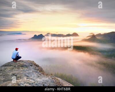 Moment de solitude sur le sommet rocheux exposés. man in black profitez d'une vue merveilleuse. s'asseoir sur le randonneur pic de roche et de regarder dans la brume et le brouillard coloré Banque D'Images