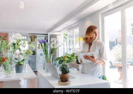 Fleuriste femme travaillant dans le magasin de fleurs avec presse-papiers et à l'extérieur de la fenêtre. Les femmes travaillant dans le magasin de fleurs. Banque D'Images