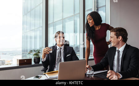Businesspeople having a conversation décontractée tout en travaillant ensemble dans le bureau. businessman sitting at table with female colleague standing by. Banque D'Images