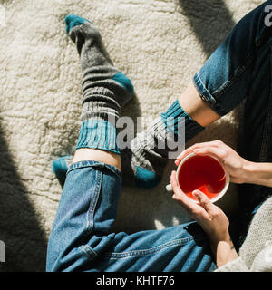 Pieds de chaussettes de laine par le Foyer de Noël. femme se détend en feu chaud avec une tasse de boisson chaude et réchauffe ses pieds en chaussettes de laine. Banque D'Images