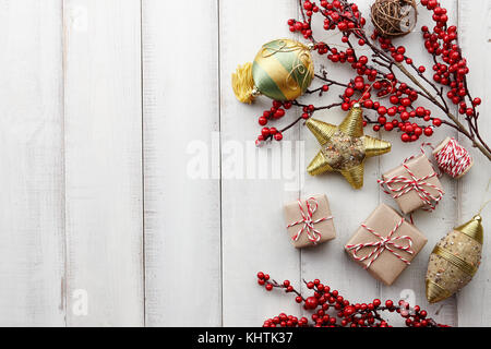 Les jouets de Noël, winterberry houx, cadeaux et coffrets cadeaux enveloppés dans du papier kraft blanc sur fond de bois, copy space Banque D'Images