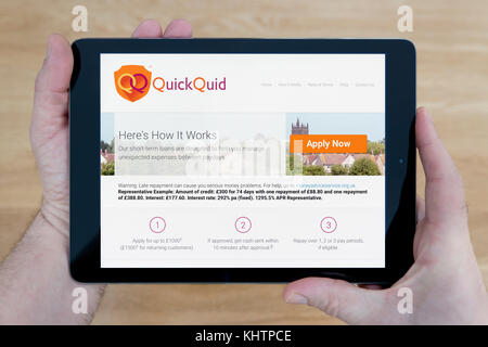 Un homme regarde le site web QuickQuid sur son iPad tablet device, tourné contre une table en bois page contexte (usage éditorial uniquement) Banque D'Images