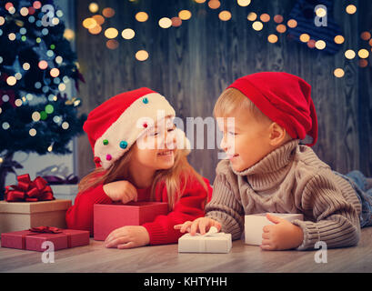 Garçon et fille se trouvant sur le plancher avec présente near Christmas Tree Banque D'Images