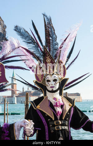 Carnaval de Venise 2017, dans l'homme à plumes masque élégant couvre-chef et devant le lagoonand San Giorgio Maggiore Banque D'Images