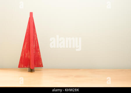 Un arbre de Noël rouge en bois stylisés avec finition en détresse assis sur une table en bois clair contre un fond vert pâle. La décoration est sur le ri Banque D'Images