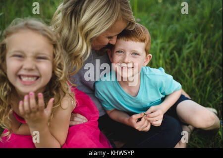 Portrait de jeune fille et son frère assis sur les genoux de la mère dans l'herbe Banque D'Images