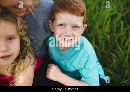 Portrait de jeune fille et son frère assis sur les genoux de la mère dans l'herbe Banque D'Images