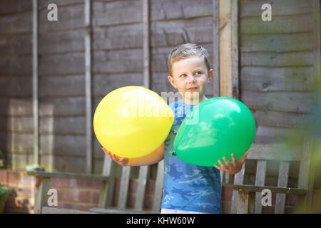 Jeune garçon en jardin, holding balloons Banque D'Images