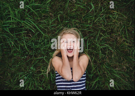 Passage portrait of girl lying on grass avec les mains sur ses joues Banque D'Images