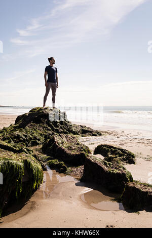Young male runner à la recherche en mer à partir de la roche de plage Banque D'Images