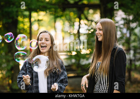 Deux jeunes amies, éclatement des bulles flottantes dans park Banque D'Images