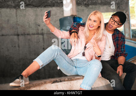 Jeune couple assis sur la rampe de skate en tenant selfies smartphone Banque D'Images