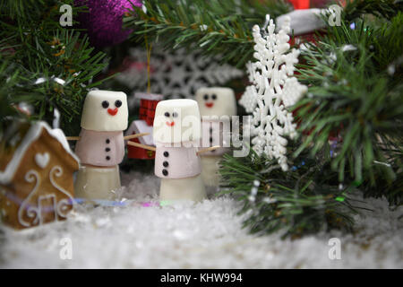 Cute noël nourriture photographie image à l'aide de guimauves en forme de bonhomme avec sourire heureux sur glacé et debout dans la neige avec un arbre de Noël Banque D'Images