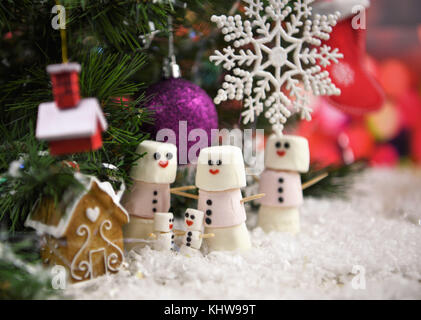 Cute noël nourriture photographie image à l'aide de guimauves en forme de bonhomme avec sourire heureux sur glacé et debout dans la neige avec un arbre de Noël Banque D'Images