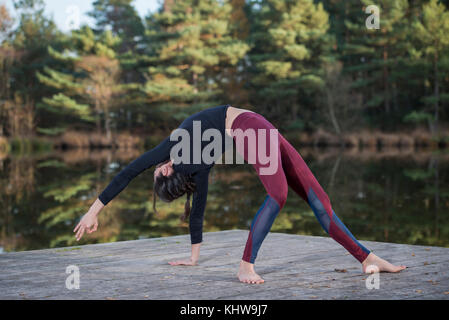 Woman practicing yoga par un lac faire un "wild thing' back bend poser. Banque D'Images