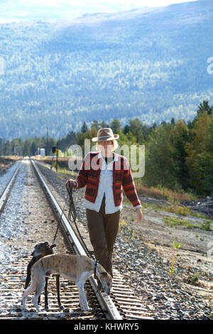 Boho girl in native style chapeau avec deux chiens l'équilibre entre les voies de chemin de fer avec des montagnes et des pins à l'arrière-plan sur une journée ensoleillée. Banque D'Images