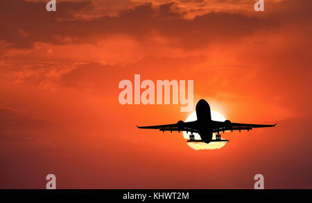 Silhouette d'avion à l'atterrissage et du ciel avec soleil. Paysage avec un avion de passagers est volant dans le ciel avec des nuages au coucher du soleil. Billet d'arrière-plan. Banque D'Images