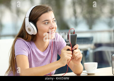 Happy teen l'écoute de musique à partir d'un smart phone portant des écouteurs et à la recherche à côté dans un café Banque D'Images