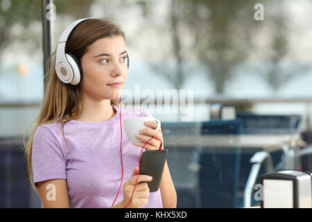 Adolescent sérieux d'écouter de la musique tenant une tasse de café et un téléphone intelligent dans un bar Banque D'Images