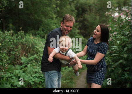 Pregnant couple swinging petit garçon sur pathway Banque D'Images