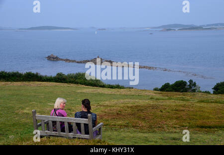 Deux femmes sur banc en bois,de parler et d'admirer la vue près de halangy village & chambre funéraire sur l'île de St Marys dans les îles Scilly, au Royaume-Uni. Banque D'Images