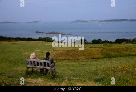 Deux femmes sur banc en bois,de parler et d'admirer la vue près de halangy village & chambre funéraire sur l'île de St Marys dans les îles Scilly, au Royaume-Uni. Banque D'Images