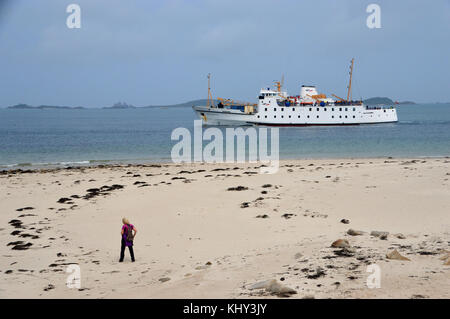 Femme seule marche sur la plage de la pointe bar comme le srr scillonian iii laissez-passer de traversier en-route de penzance à St Mary's, îles Scilly, Cornwall, UK. Banque D'Images