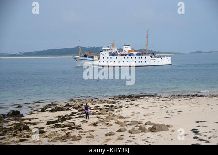 Femme seule marche sur la plage de la pointe Bar comme le SRR Scillonian III laissez-passer de traversier en-route de Penzance à St Mary's, Îles Scilly, Cornwall, UK. Banque D'Images