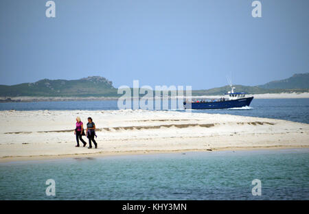 Deux femme marche sur la plage de la pointe bar sur St Marys comme le ferry (Saphir) passe sur la route de St Martins sur les îles Scilly, Cornwall, UK. Banque D'Images