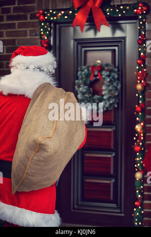 Père Noël avec de gros sac en face de la maison décorée, vue arrière Banque D'Images